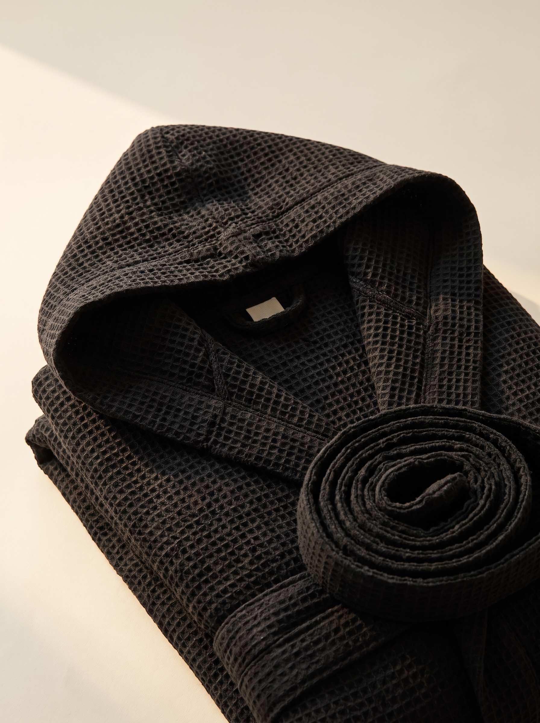 Détail de la capuche et de la ceinture du peignoir en coton gaufré noir, texture nid d'abeille