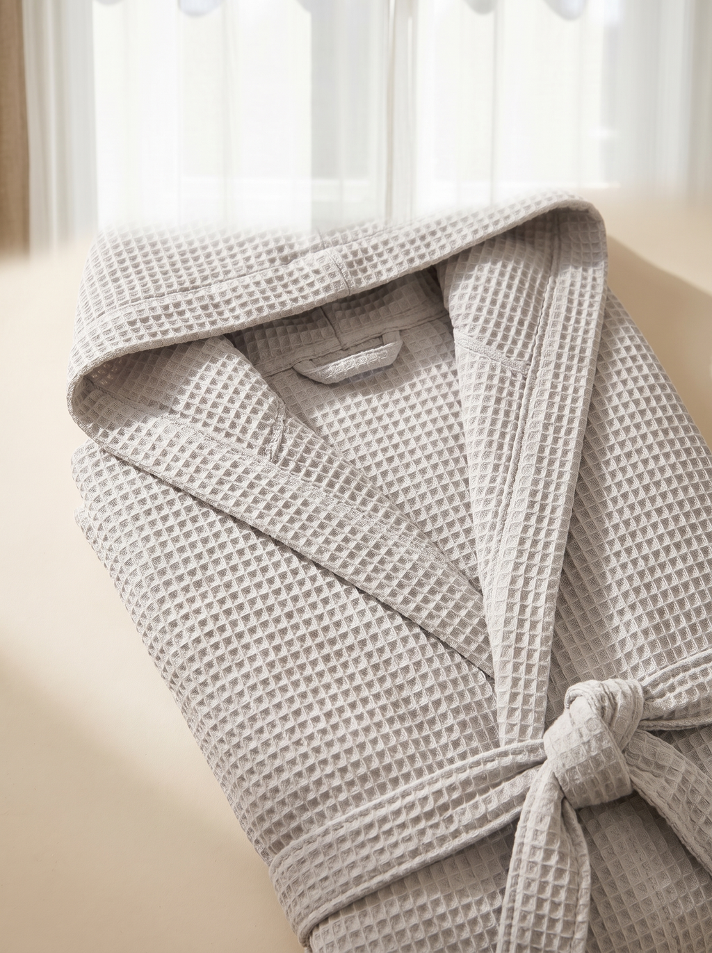 Détail de la capuche et de la ceinture du peignoir en coton gaufré gris clair, texture nid d'abeille